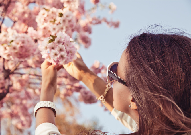 Happy woman enjoying nature. Girl with sakura tree flowers. Focus on face. Spring concept