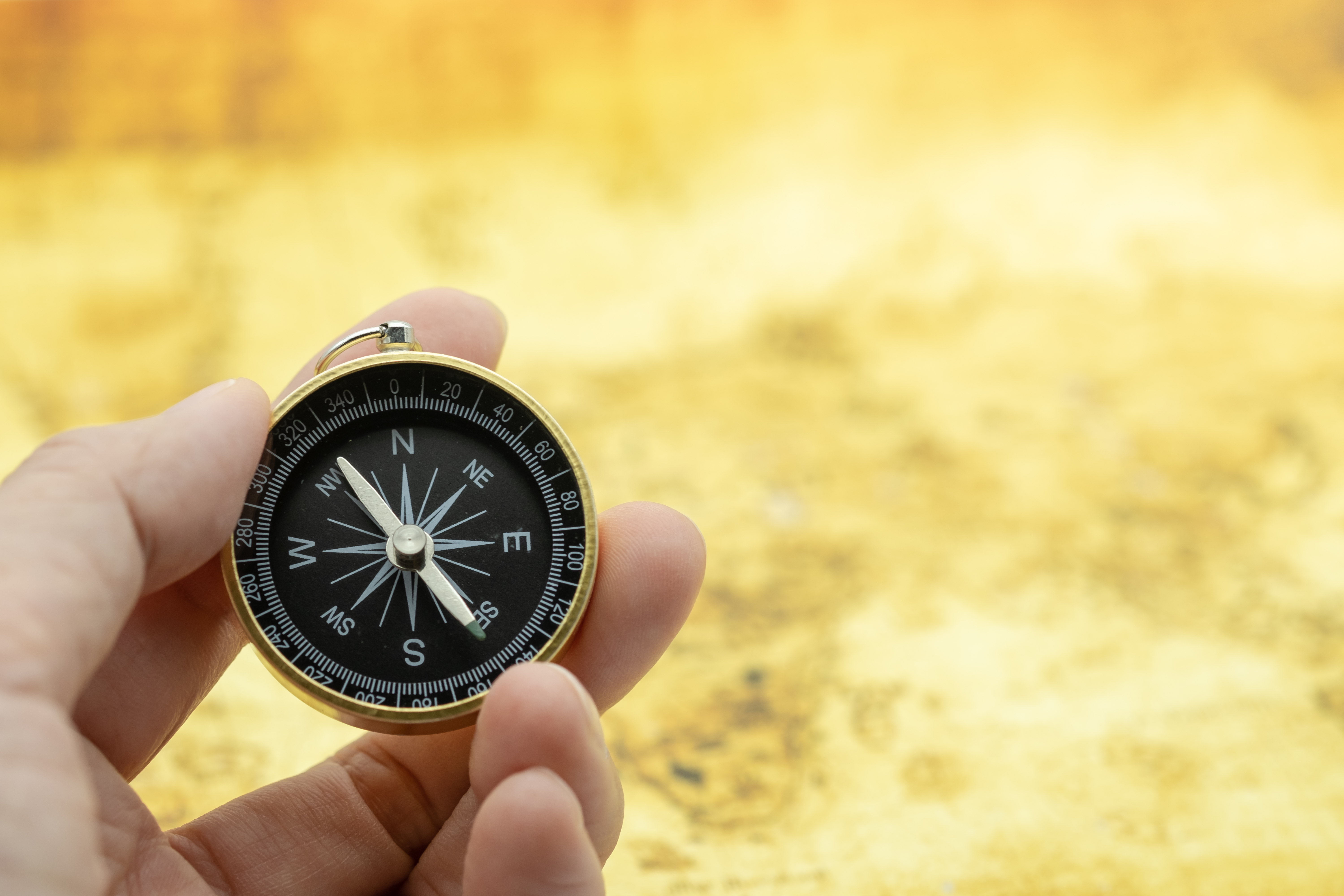 Travel and Business planning concept. Close up of man hand holding vintage compass with world map as background.