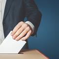 Unrecognizable male voter holds in his hand a ballot above the ballot box