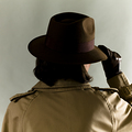 Woman in Indiana Jones style hat, London Fog overcoat and leather gloves.