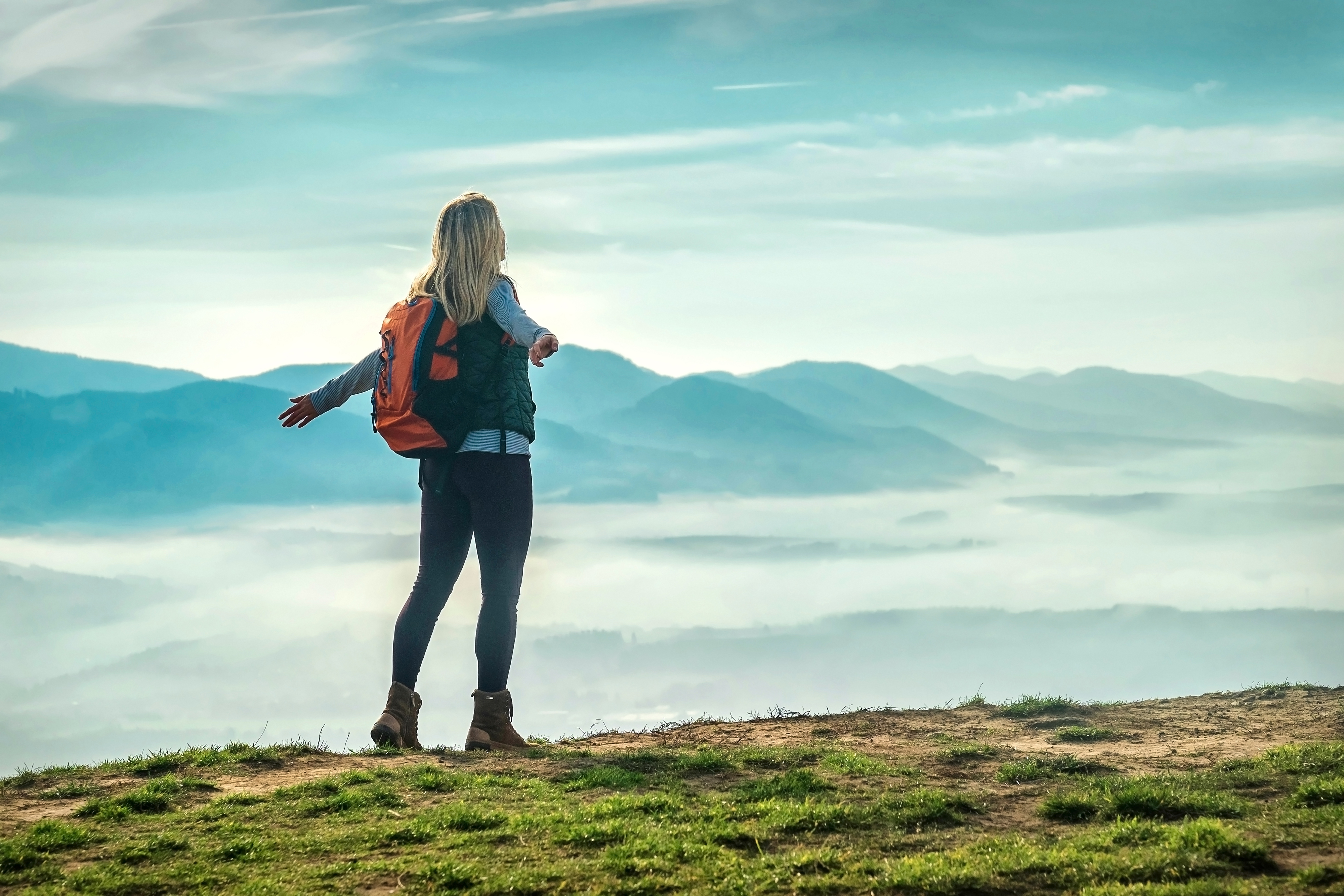 Happy woman tourist stay on the green grass on the peak of mountain and look on the nice fog view. Concept freedom.