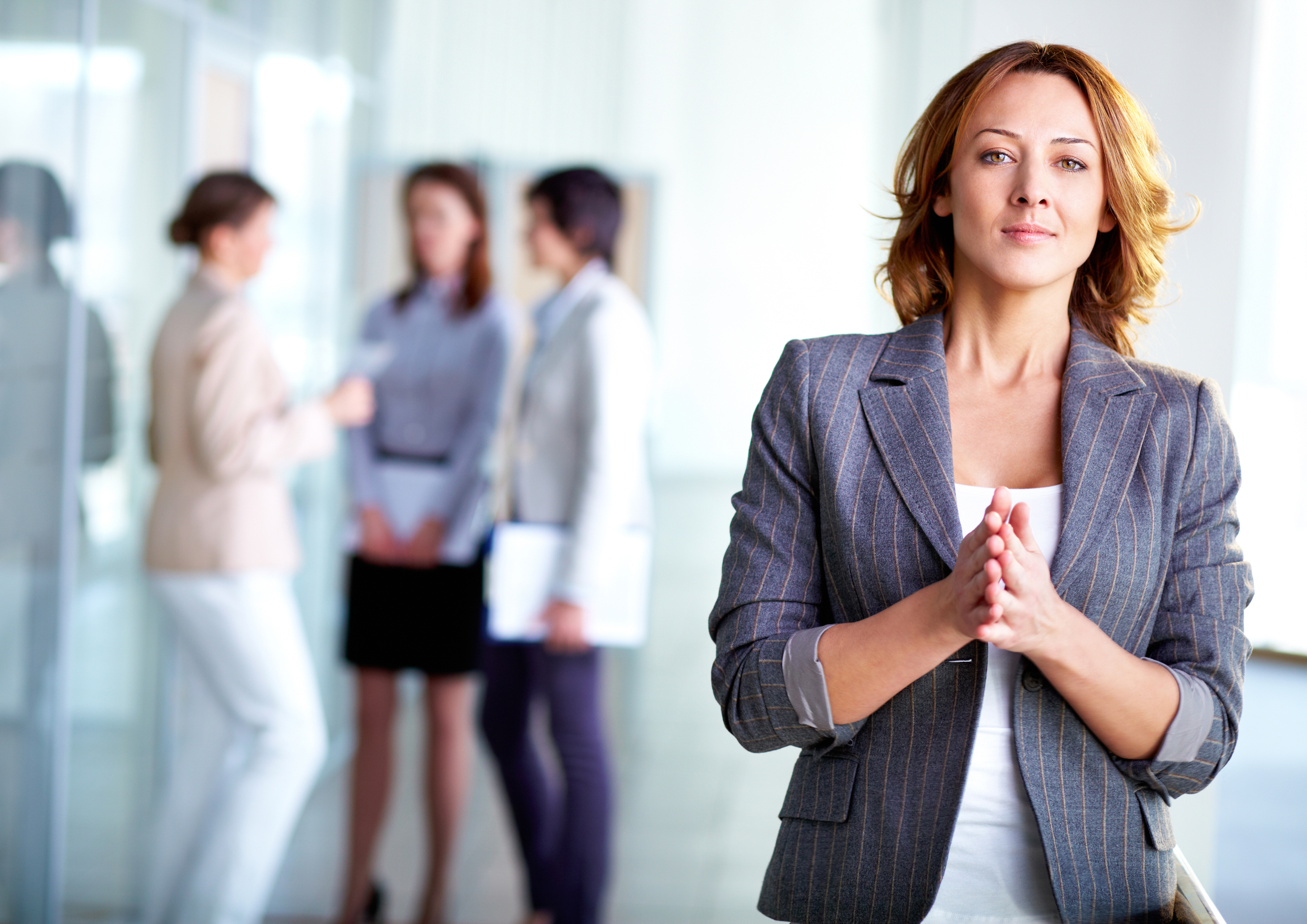 Image of pretty business leader looking at camera with interacting partners at background