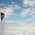 Businessman on a ladder high into the sky watching with binoculars