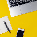 Workspace of freelancer, blogger, journalist - laptop, notepad, pen, coffe cup, smartphone on bright yellow background, top view, flat lay, copy space