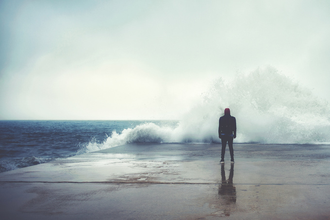 Feeling of freedom, back view of adult man standing on pier facing to the sea with big waves beats against the shore on a cloudy autumn day, alone depress person,the power of nature, storm on seashore